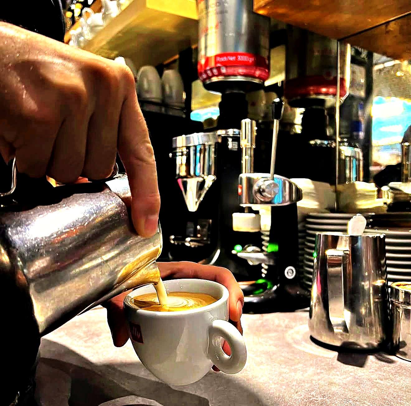 Barista gießt Milchschaum in einen Espresso in einer illy-Tasse
