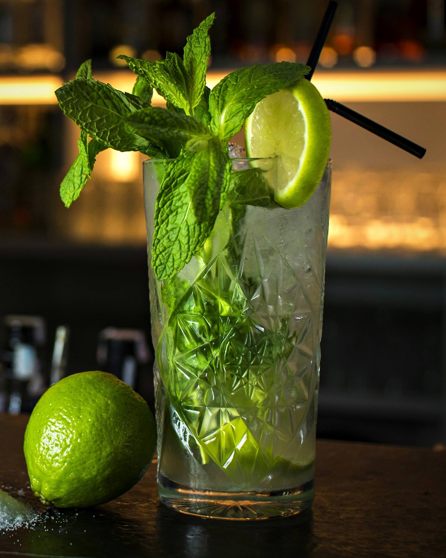 Mojito mit Minze und Limette im geschliffenen Glas an einer Bar in warmem Licht