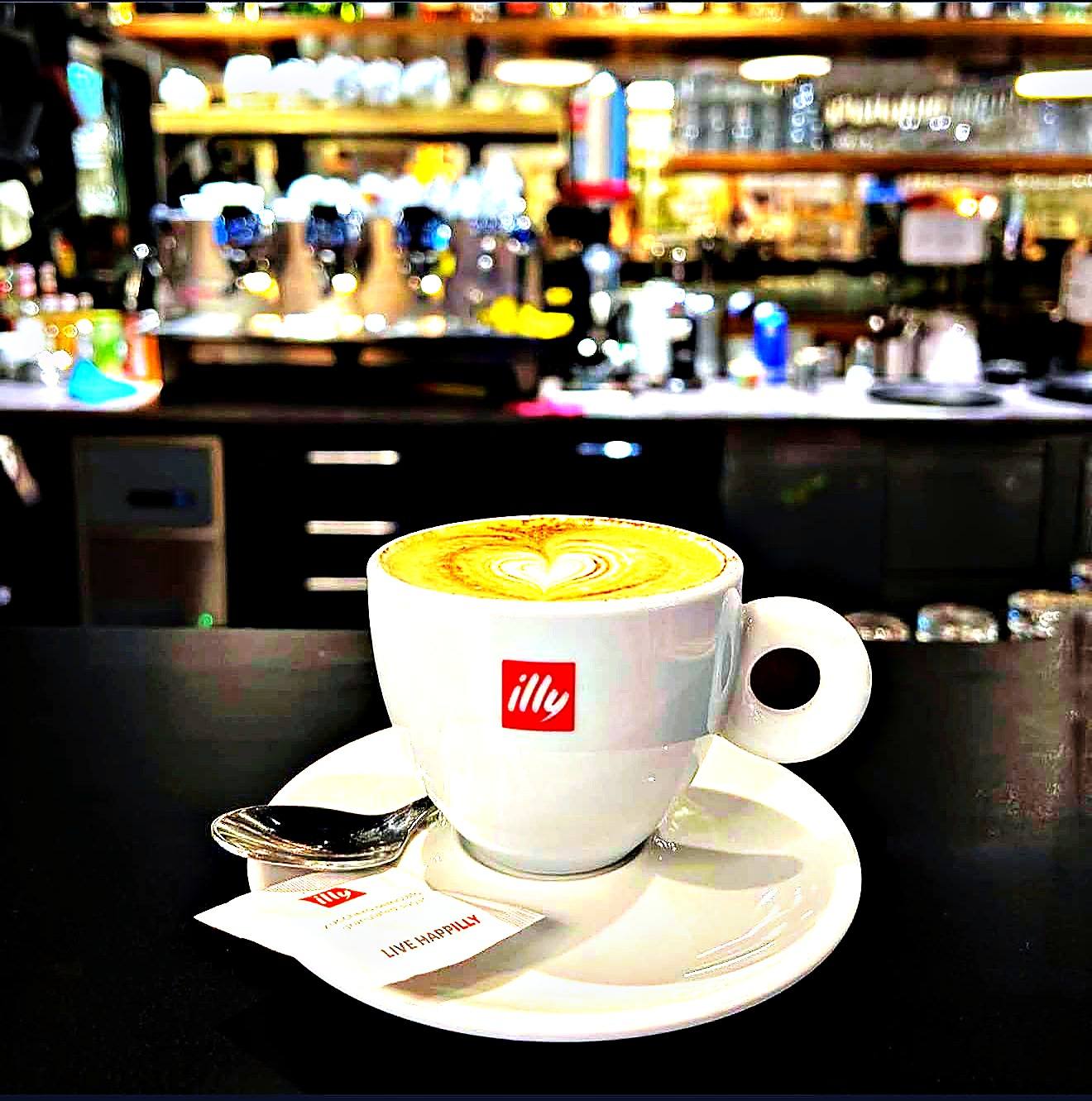 Cappuccino mit Latte-Art-Herz in einer illy-Tasse vor der Bar