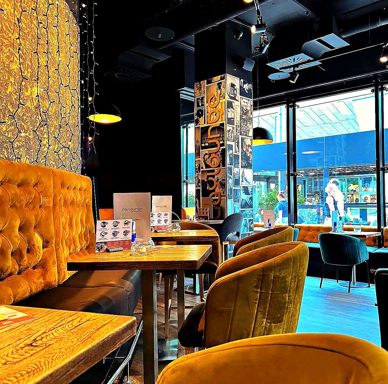 Die Lounge der daylounge: senfgelbe Samtbänke, Holztische und große Fenster zum Center Wien Mitte
