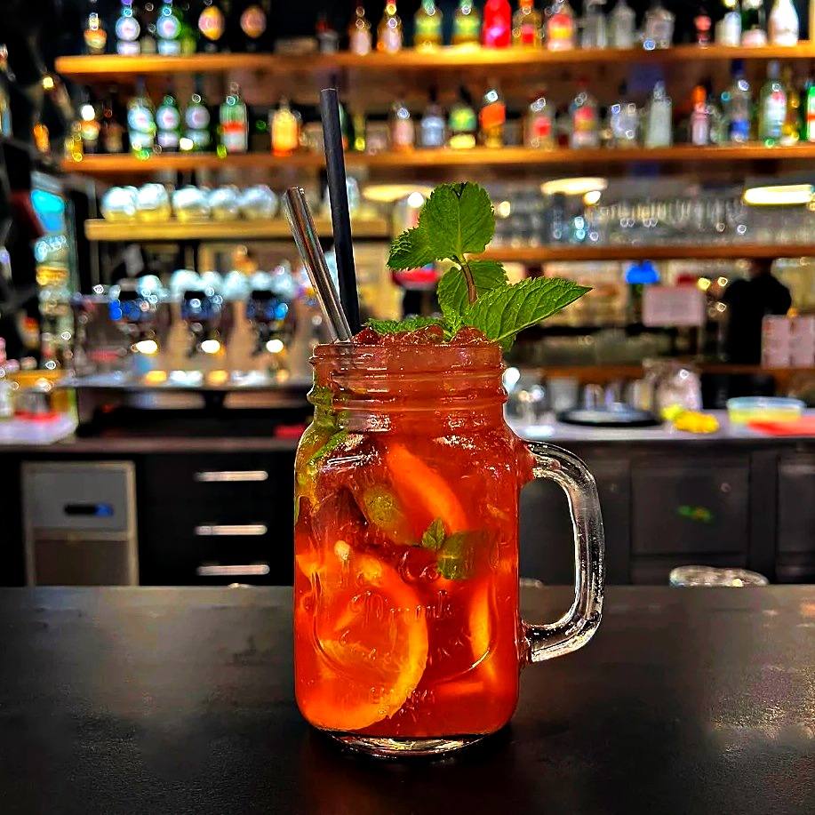 Rote Limonade mit Orangenscheiben und Minze im Henkelglas vor der Bar